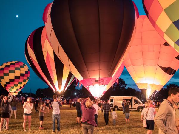 Multicolored hot air balloons are illuminated by their torches at dusk as spectators look on at the Lancaster Balloon Fest.