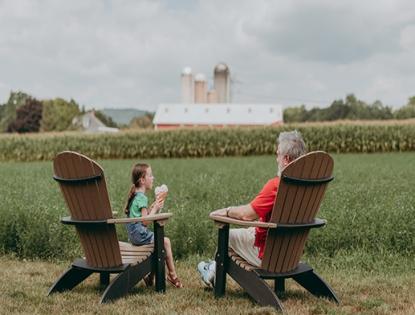 Grandchild and Grandparent sitting on lawn chairs eating ice cream while looking at farmland