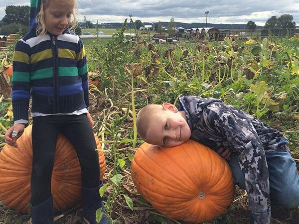 Two children sit on large pumpkins in a pumpkin patch in Lancaster, PA