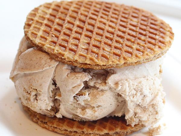 A large scoop of ice cream sandwiched between two thin stroop waffles.